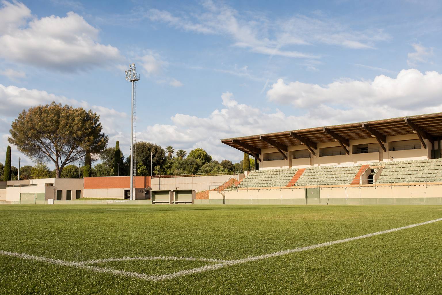 Terrain de stade Bouissou avec pelouse verte tribunes métalliques projecteurs et ciel bleu ambiance sport locale